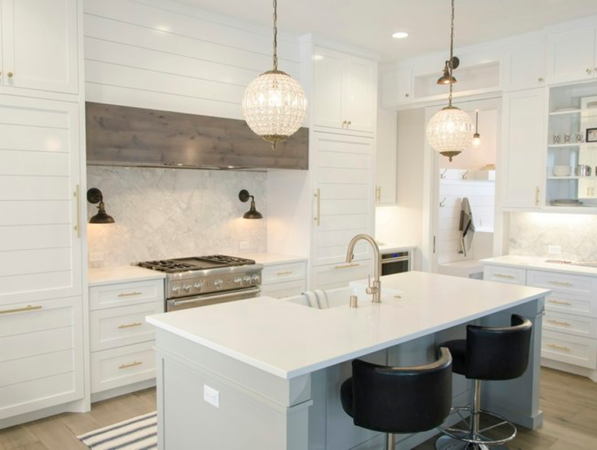 Kitchen with white countertops and cabinets. Spacious kitchen island, golden fixtures, a custom range hood vent, and a built in refrigerator.