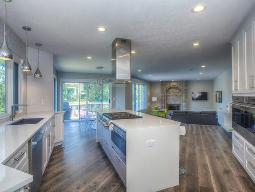 Kitchen with large white kitchen island, range hood vent, electric cooktop stove, and white quartz countertops.
