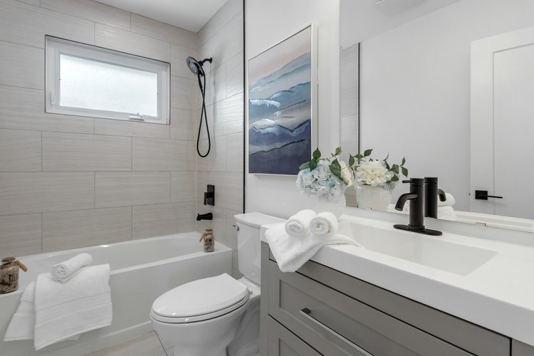 A remodeled tub and shower. Large format tile, matte black fixtures, and a gray shaker vanity.