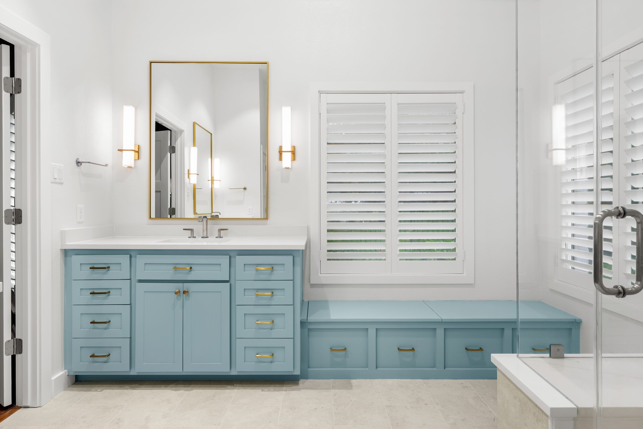 Elegant master bathroom with baby blue shaker vanities, champagne bronze fixtures, mixed metals, and natural light streaming in.
