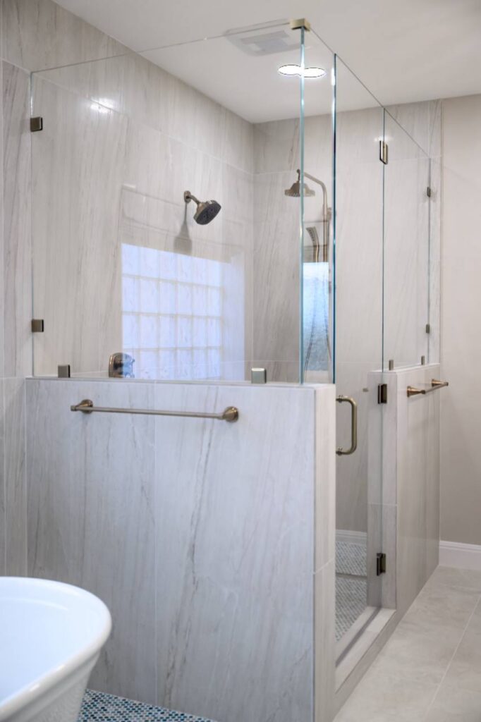Spanish Oak shower enclosure with marble-look tile, brass trim, mosaic floor