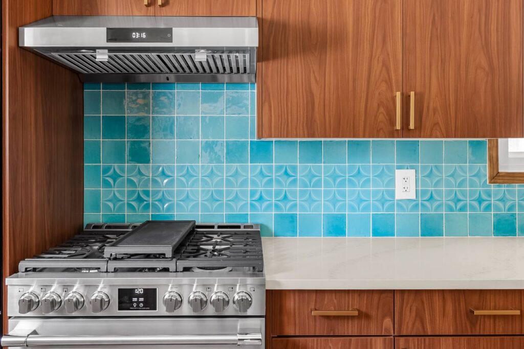 E 18th Street stove wall with turquoise patterned tile, walnut cabinetry, stainless hood