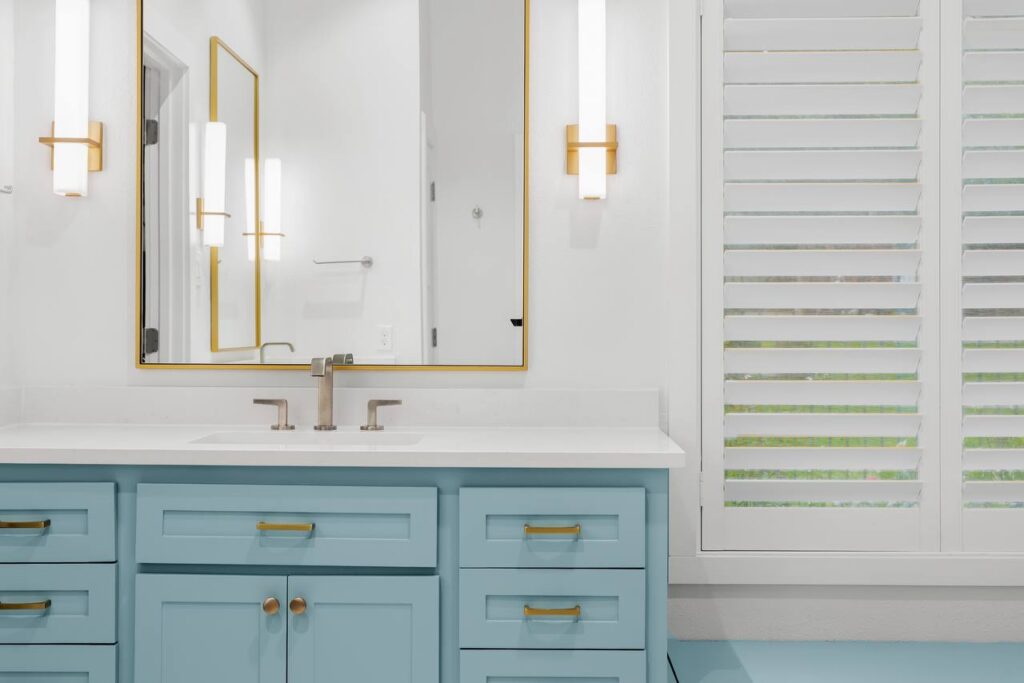 Hedgebrook Way bathroom mirrors, sconces, and plantation shutters over blue vanity