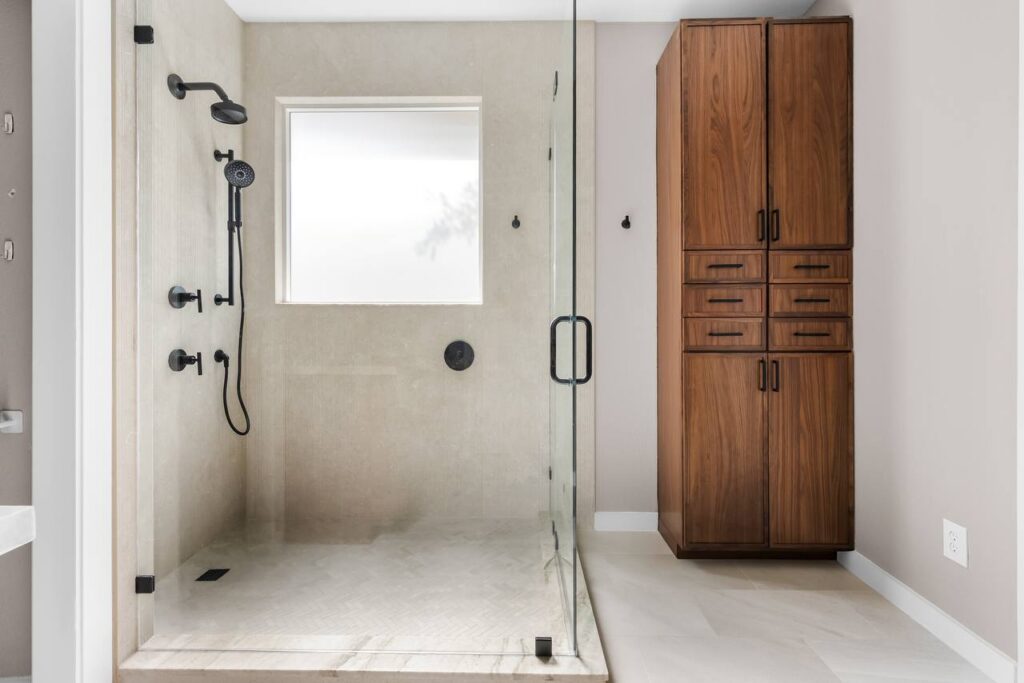 Annadale Dr. primary shower with glass enclosure, beige tile, matte black fixtures